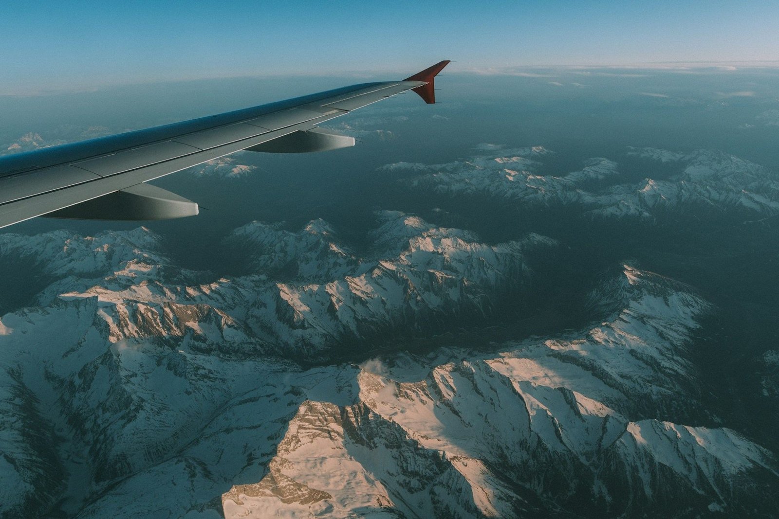 Aircraft wing over snow-capped mountains seen from a window seat