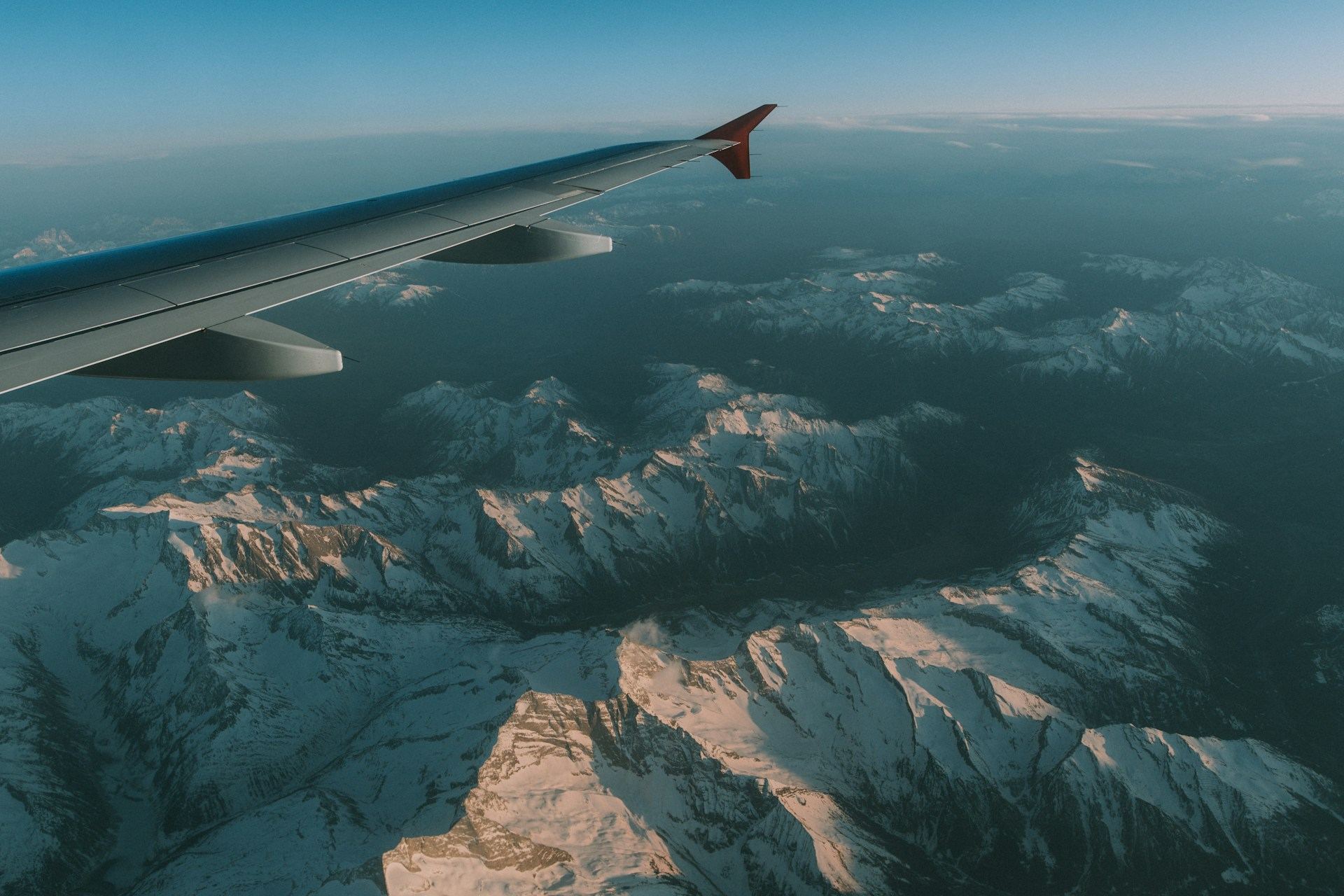 Aircraft wing over snow-capped mountains seen from a window seat
