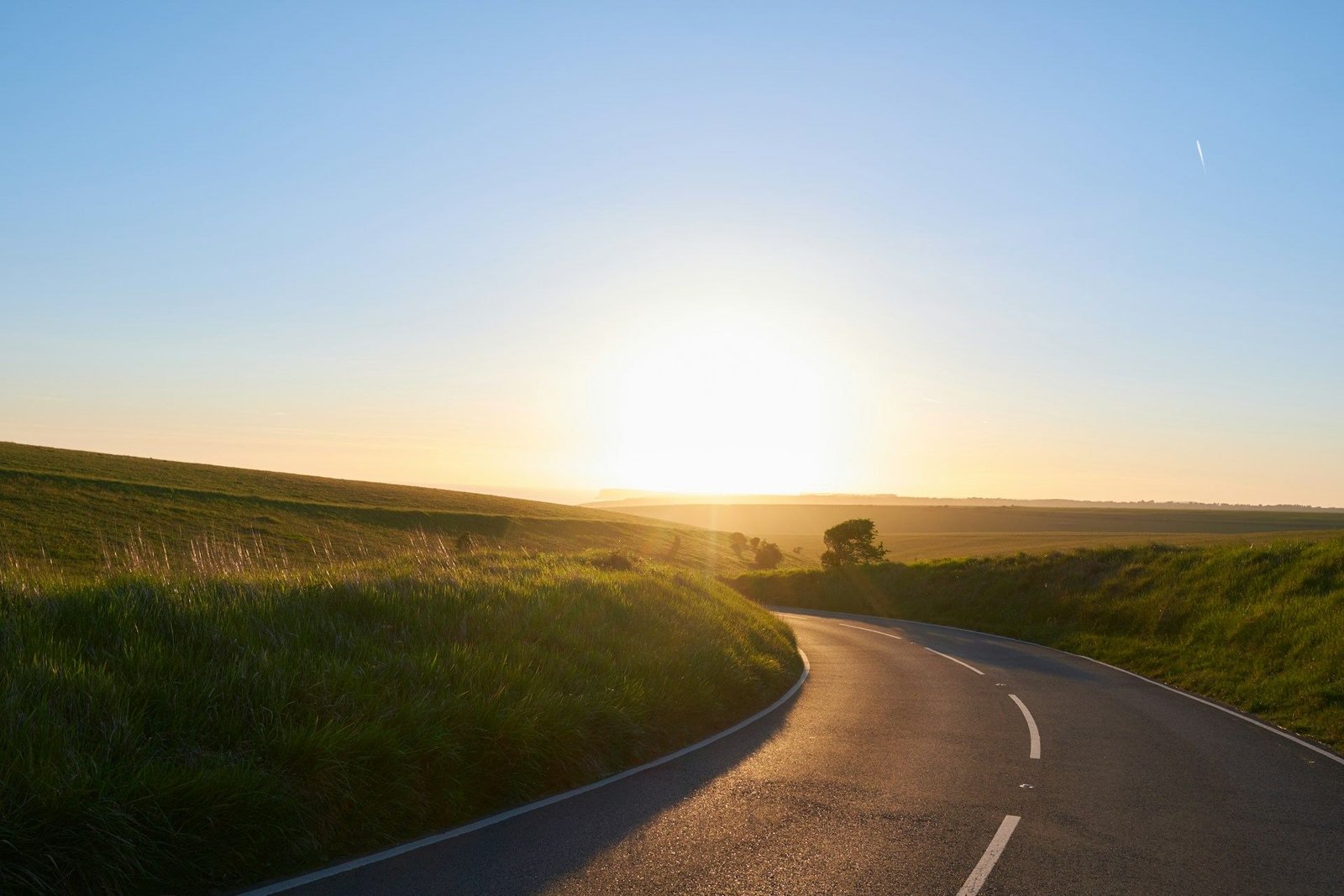 Empty country road curving towards the setting sun