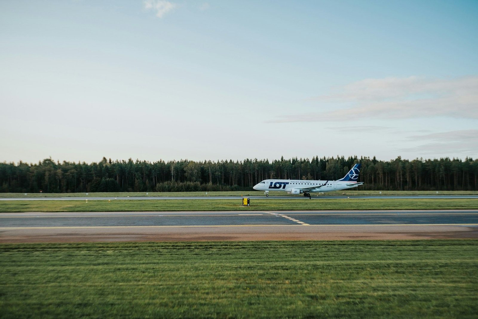 LOT Embraer jet on a runway lined with trees